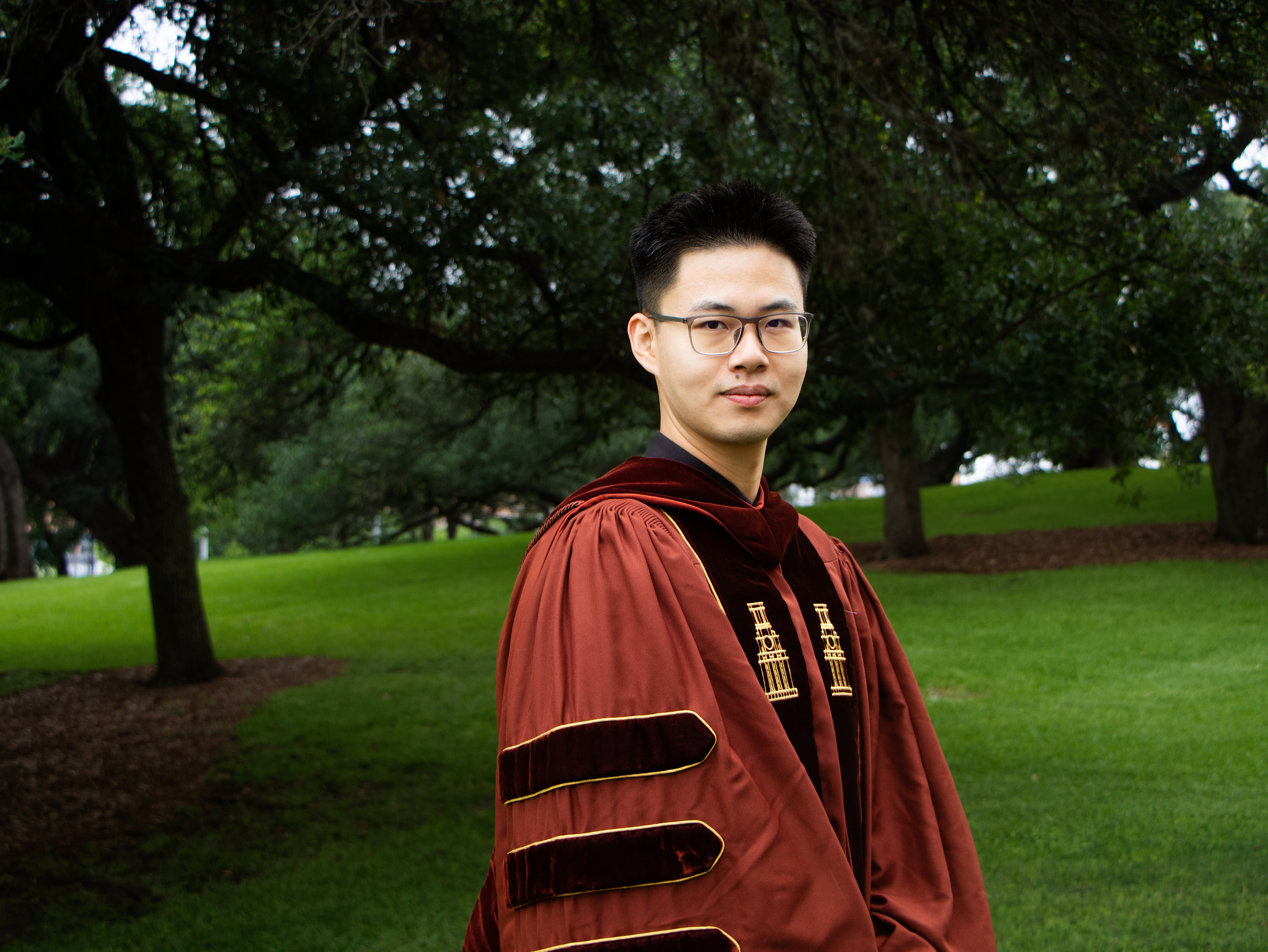 Hongli Zhan in doctoral regalia under trees