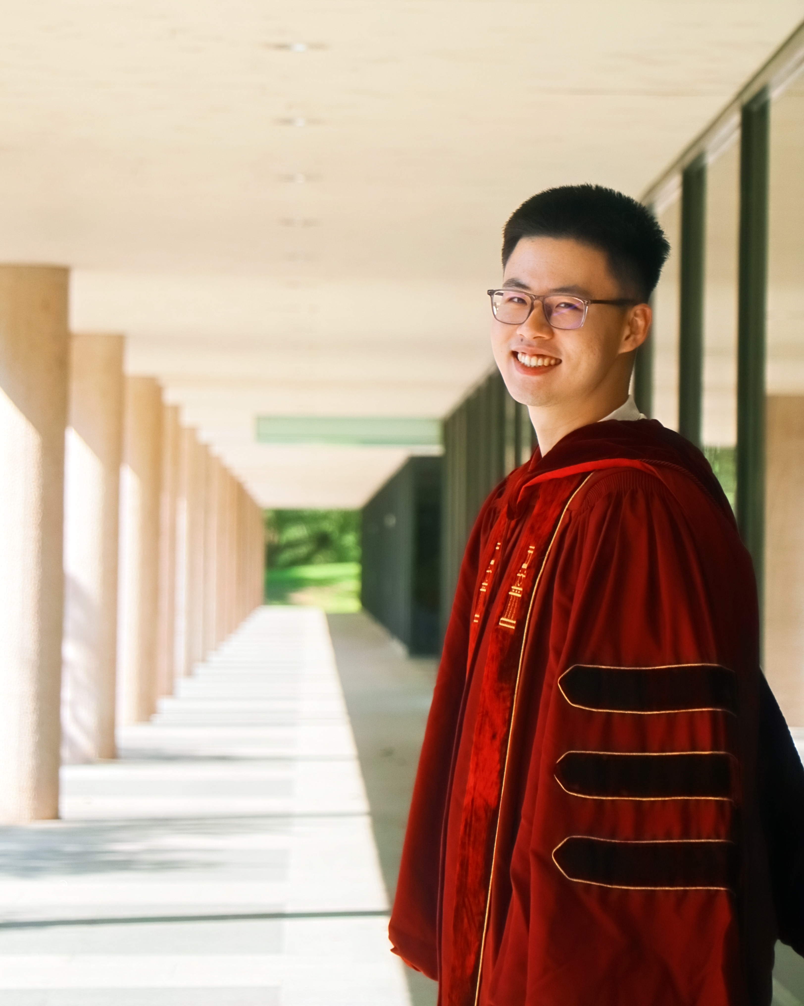 Hongli Zhan in doctoral regalia near campus columns